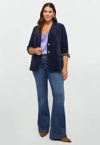 Granatowa aksamitna marynarka z złotymi guzikami i wzorzystym mankietem, w połączeniu z lawendową koronkową bluzką bez rękawów oraz dżinsami w stylu dzwonów. Brązowe szpilki w szpic.