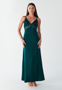 Lungo abito in satin color tè con spalline sottili, dettagli in pizzo in vita e una silhouette fluida e morbida. Indossato con sandali color nude.