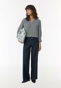 Schwarz-weiß gemusterte Bluse mit V-Ausschnitt, kombiniert mit dunkelblauen, weit geschnittenen Jeans mit Kontrastnähten und einer silbernen Tasche.