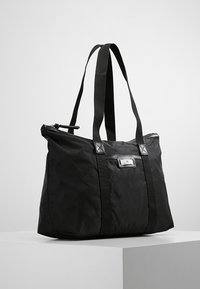 Zwarte nylon draagtas met dubbele stevige handvatten, ritsluiting en een platte vorm. Bevat een rechthoekig logo-opdruk aan de voorkant.