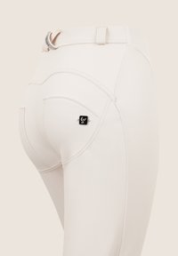 Pantalons rose clair en tissu extensible, avec taille haute, coutures courbes et une étiquette de marque noire sur la poche arrière.