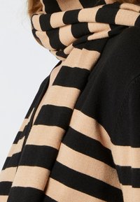 Pletená šála s střídavými černými a béžovými vodorovnými pruhy. Měkká textura, střední šířka, volný styl omotání.