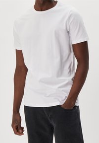 Weißes T-Shirt mit Rundhalsausschnitt aus Baumwolle, mit normaler Passform und kurzen Ärmeln. Kombiniert mit dunkelgrauen Jeans. Einfaches, einfarbiges Design.