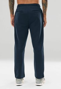 Mørkeblå joggingbukser med snøre i taljen, sidelommer og en afslappet pasform. Stoffet fremstår blødt med en glat overflade.