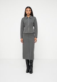 Ensemble en maille grise composé d'une veste zippée à col et d'une jupe longue assortie, associé à des bottes noires jusqu'aux genoux.