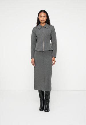 Pilkos megztos dviejų dalių aprangos, kurią sudaro apykakle su užtrauktuku ir derančios ilgos sijonas, derinamos su juodais iki kelių batais.