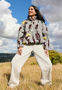 Gray fleece zip-up jacket with floral and vine textures in burgundy, yellow, and green. Paired with wide-leg light gray pants.