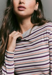 Striped long-sleeve top featuring gray, purple, and orange horizontal lines. Soft ribbed texture with a cowl neckline. Hand gently touching collar.
