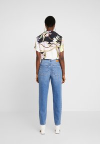 Blommönstrad skjorta med korta ärmar och en svart sektion, tillsammans med högmidjade blå denimjeans och vita klackboots.