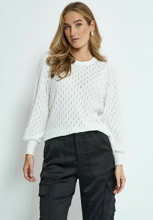 Maglione lavorato a maglia bianco con motivo a diamante, collo rotondo e maniche lunghe. Abbinato a pantaloni cargo neri in satin con tasche.