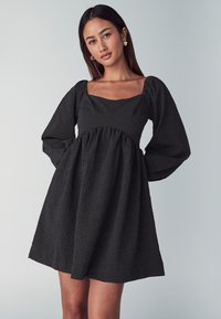 Schwarzes, strukturiertes Mini-Kleid mit quadratischem Ausschnitt, gepufften langen Ärmeln und gerafftem Taillenbereich, das eine ausgestellte Silhouette aufweist.