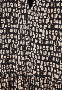 Juoda suknelė su kreminiu geometriniu raštu, turinti mygtukų užsegimą ir banguotą apatinę dalį. Pagaminta iš minkštos, tekstūruotos medžiagos.