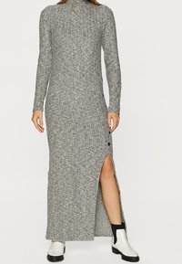 Graues geripptes Maxikleid aus Strick mit langen Ärmeln, hohem Ausschnitt, seitlichem Schlitz, Knopfdetail und kombiniert mit schwarz-weißen Ankle Boots.
