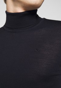 Maglione a dolcevita nero in tessuto a coste con un design aderente, caratterizzato da un logo ricamato discreto sul petto.