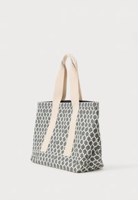 Geometrikus mintázatú táska sötétkék és krémszínben, bézs szövetfogantyúkkal és strukturált kialakítással. Texturált felület.