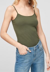 Olijf groene tanktop met dunne bandjes, gemaakt van zachte stof. Gecombineerd met lichtblauwe denim jeans, met voorzakken en een slim fit.