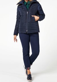 Námořnická prošívaná bunda se zipem, dvěma předními kapsami a kapucí. V kombinaci s tmavými džíny s kostkovaným vzorem na manžetách a námořnickými botami.