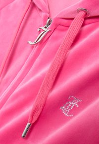 Roze velours hoodie met een zilveren rits met logo trekker, textuur trekkoorden en strassdetail op de voorkant. Zachte stofafwerking.