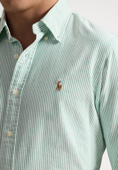 Short-sleeve button-up shirt made of light green fabric with fine white stripes. Features a small, embroidered horse logo on the chest.