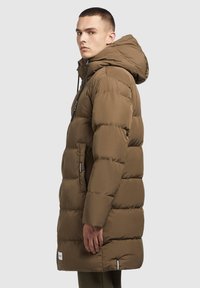 Külastus jope oliivrohelises värvis, varustatud kapuutsiga, tikandiga disain, lukuga sulgemine, kaks külgmist taskut ja logode aktsendid kangal.