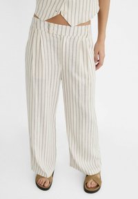 Lniane spodnie o szerokich nogawkach z pionowymi beżowo-szarymi paskami. Posiadają zakładki i dwa przednie guziki. Miękka tekstura i luźny krój.