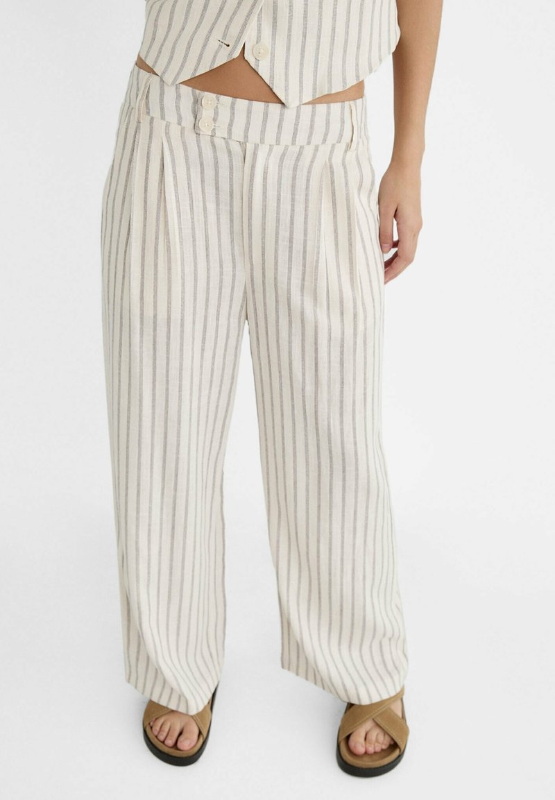 Lniane spodnie o szerokich nogawkach z pionowymi beżowo-szarymi paskami. Posiadają zakładki i dwa przednie guziki. Miękka tekstura i luźny krój.