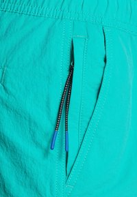 Aqua színű úszónadrág, könnyű anyagból készült, rugalmas derékkal, oldalsó zsebbel és kontrasztos kék húzózsinórral, fekete akcentussal.