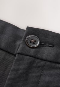 Gros plan sur un tissu noir avec un bouton à quatre trous cousu près d'une boutonnière cousue sur un vêtement sur mesure.