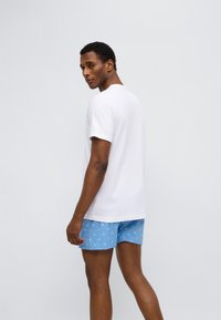 Άσπρο κοντομάνικο t-shirt συνδυασμένο με ανοιχτό μπλε μαγιό σορτς με επαναλαμβανόμενο μικρό λευκό μοτίβο. Ομαλό ύφασμα, άνετη εφαρμογή.