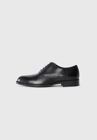 Chaussure de cérémonie pour homme en cuir noir avec laçage fermé, bout arrondi, petit talon et finition lisse et polie sur un fond blanc.