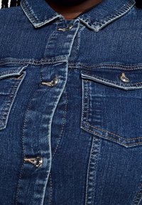 Jeansskjorta i en mörkblå tvätt, klassisk krage, knappfront och två bröstfickor med metallelement. Strukturerad tyg och sömdetaljer.