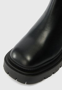 Black leather ankle boot with smooth upper, rounded toe, and chunky rubber sole featuring a textured tread pattern.