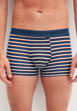 Boxer aderenti blu navy con righe orizzontali in rosso, giallo e bianco. Tessuto morbido con una fascia in vita strutturata che reca il nome del marchio.