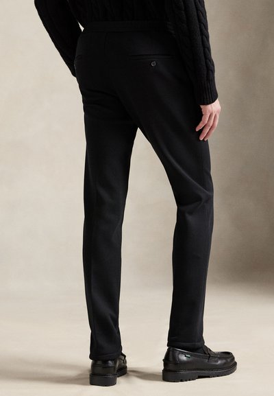 Μαύροι μάλλινοι παντελόνια με εφαρμογή κοψίματος, με λεία υφή, δύο πίσω τσέπες και συνδυασμένοι με μαύρα μοκασίνια.