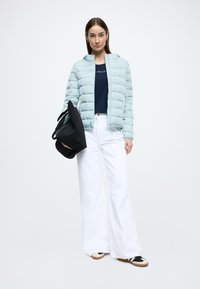 Ανοιχτό μπλε μπουφάν puffer με κουκούλα, κλείσιμο με φερμουάρ, συνδυασμένο με μπλε σκούρο τοπ και λευκό παντελόνι με φαρδιά μπατζάκια. Μαύρη τσάντα και casual παπούτσια συμπεριλαμβάνονται.