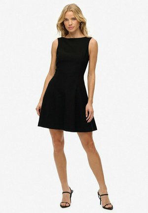 Vestido negro sin mangas con un torso ajustado y falda acampanada. Textura suave, hasta la rodilla y diseño minimalista. Sandalias de tacón simples.