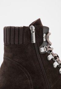 Brązowe zamszowe botki za kostkę z żeberkowym mankietem, srebrnym zamkiem błyskawicznym oraz sznurowanym fasonem z teksturowanym wykończeniem po bokach.