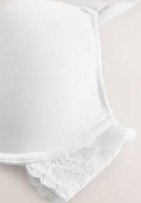White padded bra cup with delicate lace trim and adjustable strap on a light background.