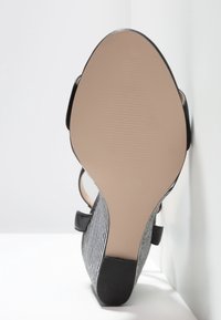Vue de la semelle d'une chaussure à talons hauts rayée noire et blanche avec une semelle beige lisse et un talon noir, positionnée sur un fond blanc.