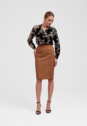 Czarna blouse w kwiaty z długimi rękawami, zestawiona z beżową spódnicą ołówkową z bocznym detalem na guzik. Dopełnieniem stylizacji są czarne sandały na obcasie.