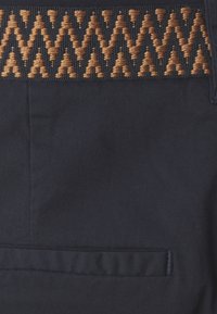 Ναυτικό ύφασμα που παρουσιάζει μια υφασμένη ζώνη με ζιγκ-ζαγκ σχέδιο σε πορτοκαλί και ανοιχτό καφέ, διαθέτοντας κρυφό πλαϊνό τσέπη.