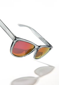 Hallid läbipaistvad päikeseprillid punaste ja oranžide üleminekuvärvusega läätsedega. Omavad kolmnurksed raamid ja bränditud käepidemeid.