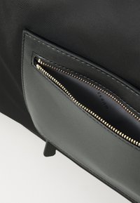 Sac à main noir avec une poche zippée et des finitions dorées, texture en cuir lisse et design minimaliste. La doublure intérieure est également noire.