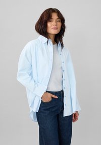Light blue button-up shirt in cotton with a relaxed fit, mixed with a gray crewneck shirt, paired with dark blue jeans.