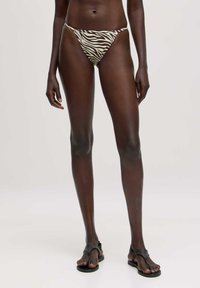 Zebra-gepatroneerde bikini onderkant in crème en bruine tinten, low-rise ontwerp, dunne zijbandjes, gecombineerd met zwarte minimalistische sandalen.