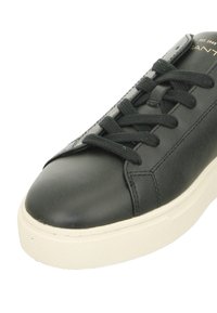 Black leather sneaker with a rounded toe, textured surface, flat laces, and a contrasting white rubber sole featuring a textured pattern.
