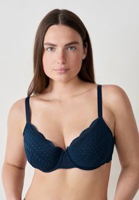 Reggiseno in pizzo blu navy con un motivo geometrico testurizzato, coppe con ferretto, spalline regolabili e bordi scallop per un tocco di dettaglio.