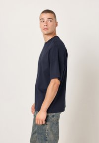 Temno modra bombažna majica z velikimi kroji, kratkimi rokavi, okrolim izrezom in sproščenim krojem, združena s svetlo modrimi kavbojkami.