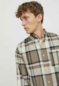 Camisa de cuadros en colores beige, blanco y negro. Presenta un bolsillo en el pecho, cuello y mangas largas con un ajuste entallado.