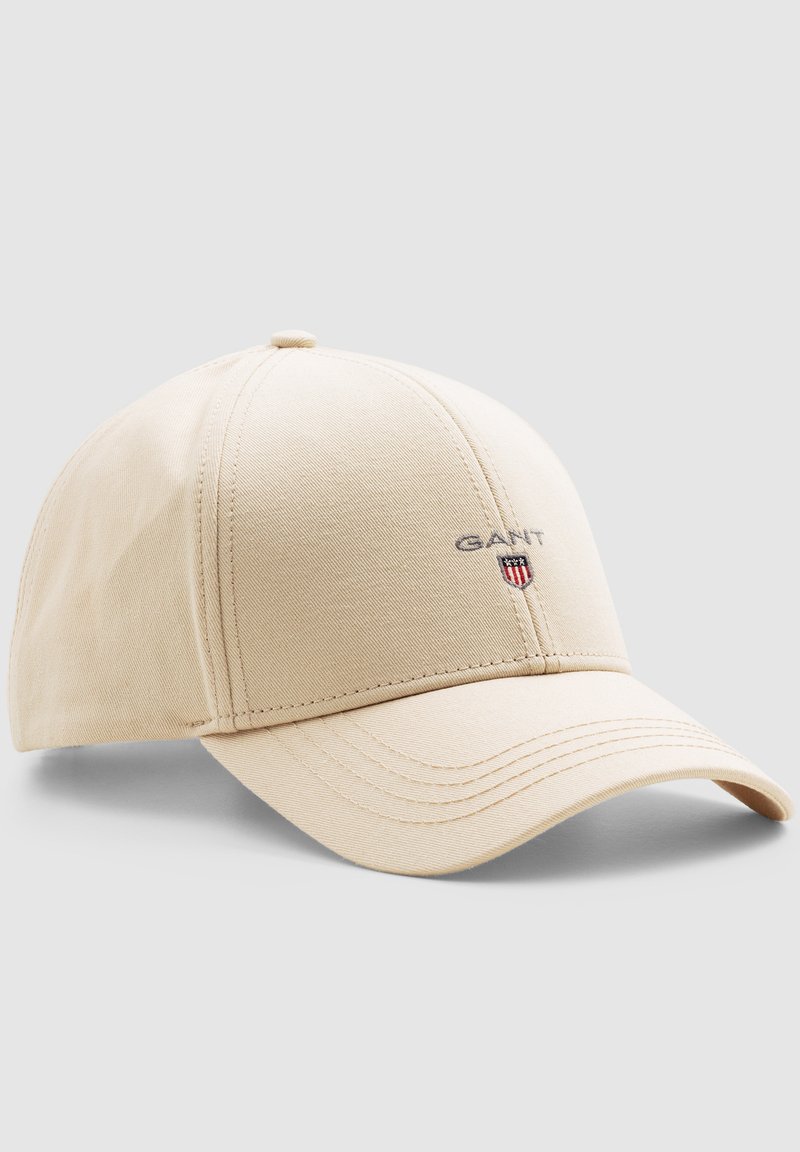Beige bomuldsbaseballcap med buet skygge, syede paneler og et lille GANT-logo med skjoldsymbol på forsiden.